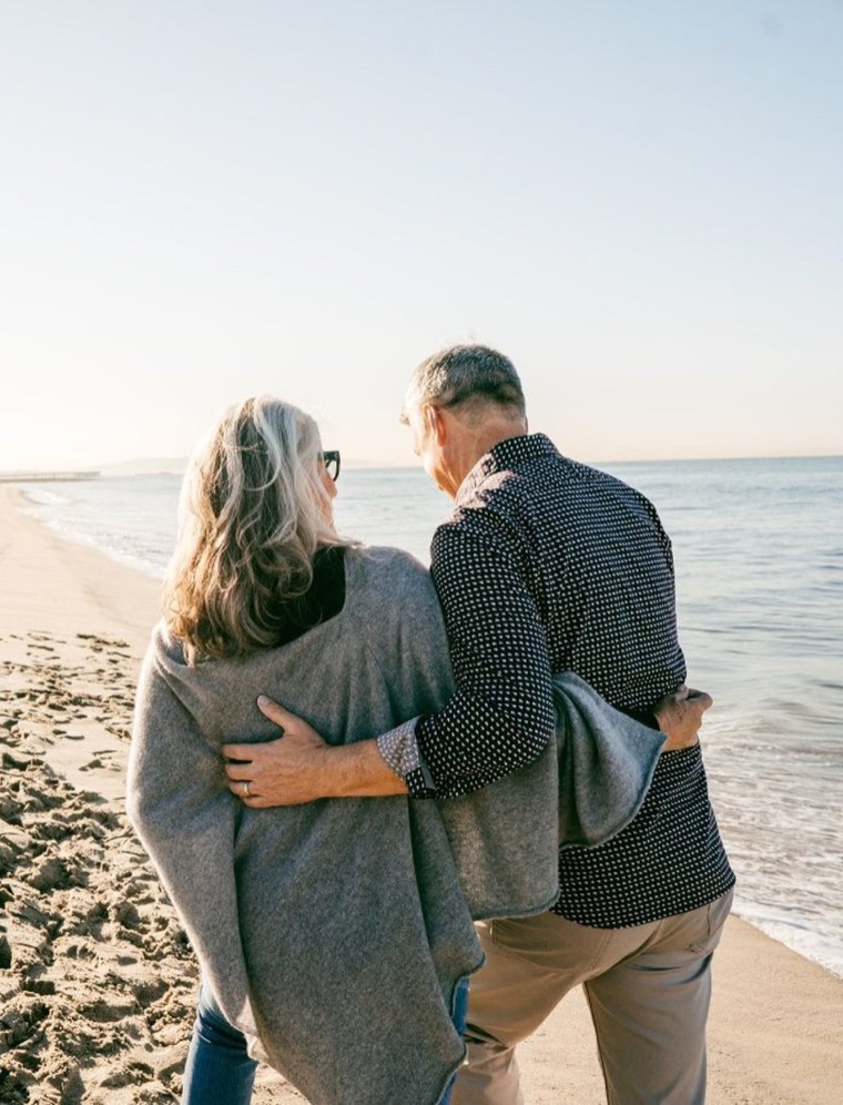 An older couple walking arm in arm along the beach at the water's edge